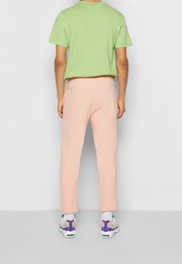 Zelené krátké bavlněné tričko, volný střih, spojené s měkkými, pastelově růžovými tepláky. Bílé a vícebarevné tenisky dokončují tento outfit.