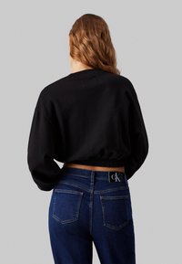Felpa nera corta con collo rotondo e orlo a coste, abbinata a jeans in denim blu con un'etichetta logo sul retro e tasche semplici.