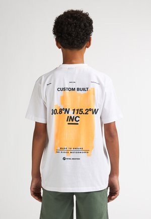 T-shirt en coton blanc avec un grand motif orange comportant du texte, manches courtes et col rond. Le dos présente des coordonnées et un logo.