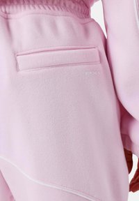 Pantalones de chándal de felpa rosa con un acabado texturizado, que cuentan con un bolsillo trasero y un logo blanco. Tejido suave con una cinturilla elástica.