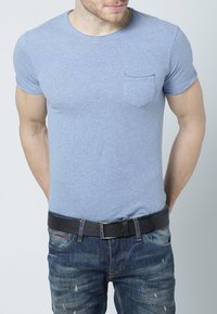 Blå kortermet t-skjorte i en blandet stoff med brystlomme, kombinert med slitte denimjeans og et svart belte.