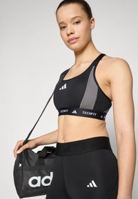 Black athletic sports bra with gray accents and a logo band, paired with high-waisted black leggings featuring a logo at the waist.