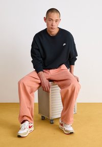 Svart oversized sweatshirt med en liten vit Nike-logga, i kombination med ljusrosa vida byxor och vita sneakers med röda detaljer.