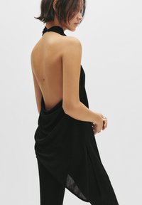 Rochie neagră fără mâneci, cu guler halter, spate descoperit, textură drapată și un finisaj lucios, având o fente laterală și un design minimalist.
