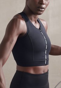 Top desportivo preto com fecho à frente, apresentando um design justo e uma textura suave, combinado com leggings de cintura alta a condizer.