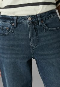 Jeans en denim bleu foncé avec taille haute, conception à cinq poches, rivets en cuivre et légères traces d'usure à l'avant.