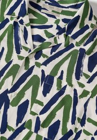 Chemise blanche à col avec une coupe décontractée présentant des motifs audacieux de coups de pinceau bleus et verts et une poche poitrine à l'avant.