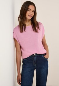 Rosa stickad tröja med korta ärmar och rundad halsringning, i kombination med mörkblå denimjeans med knappstängning och sidofickor.