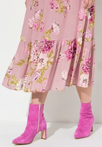 Blumenkleid aus pinkem Stoff mit großen Blumen in verschiedenen Rosa- und Grüntönen, kombiniert mit knallpinken Ankle Boots mit Blockabsatz.