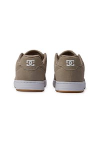 Baskets en suède beige avec semelles en caoutchouc blanc, arborant un logo blanc en évidence à l'arrière, de forme arrondie et avec un col rembourré.
