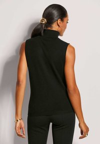 Schwarzer ärmelloser Rollkragenpullover mit glatter Textur, geripptem Saum und figurbetontem Design. Getragen mit einem passenden Outfit, das goldene Akzente aufweist.