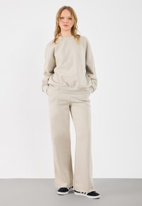 Beige sweatshirt en bijpassende wijde sweatpants gemaakt van zacht materiaal. Casual ontwerp met een ronde hals en zijzakken. Zwarte schoenen.