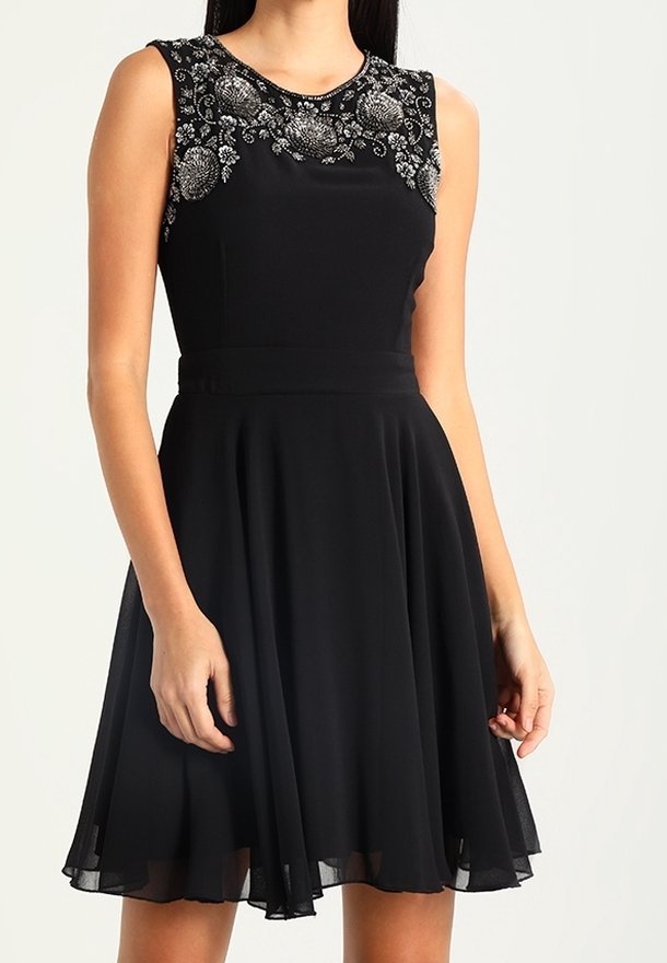 Černé šaty bez rukávů s přiléhavým živůtkem a rozšířenou sukní. Obsahují složité korálkování na výstřihu a hladkou, splývavou látku.