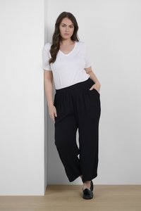 Weißes V-Ausschnitt-T-Shirt, kombiniert mit schwarzen, locker sitzenden, gefalteten Hosen mit elastischem Bund und Seitentaschen, vor einem neutralen Hintergrund.