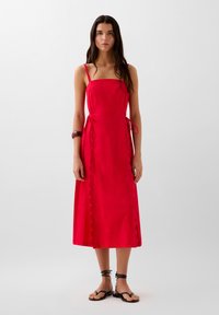 Punainen midi-mekko, jossa on spagettiolkaimet, kenttäsaumadetalji ja tiivis vyötärö. Yhdistetty mustiin remmisandaaleihin ja viininpunaisiin koruihin.