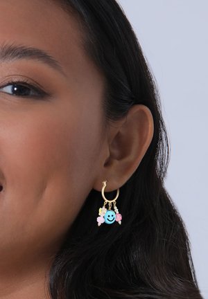 Orecchini a cerchio dorati caratterizzati da perline colorate, tra cui una faccina sorridente blu, accenti rosa e gialli, e dettagli testurizzati, appesi al cerchio.