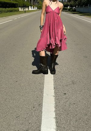 Różowa sukienka z falbanami, cienkimi ramiączkami, luźnym dołem i subtelnym wykończeniem; zestawiona z czarnymi, skórzanymi kozakiem do kolan z klamrami.