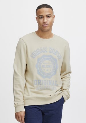 Light beige sweatshirt with long sleeves, round neckline, and a printed blue graphic reading "URBAN CREW ORIGINAL." Soft texture, casual fit.