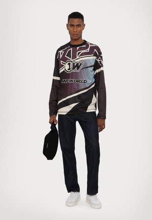 Long-sleeve graphic shirt in dark tones with blue gradient, featuring bold designs and logos. Paired with dark jeans and white sneakers.