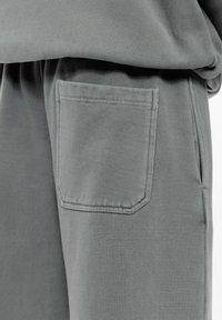 Szare dresy wykonane z miękkiego materiału, z elastycznym pasem i jedną kieszenią naszywaną po prawej stronie.