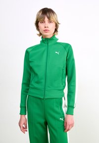 Green zip-up track jacket with ribbed collar, featuring white stripes along sleeves. Logo embroidered on chest, made of smooth athletic fabric.