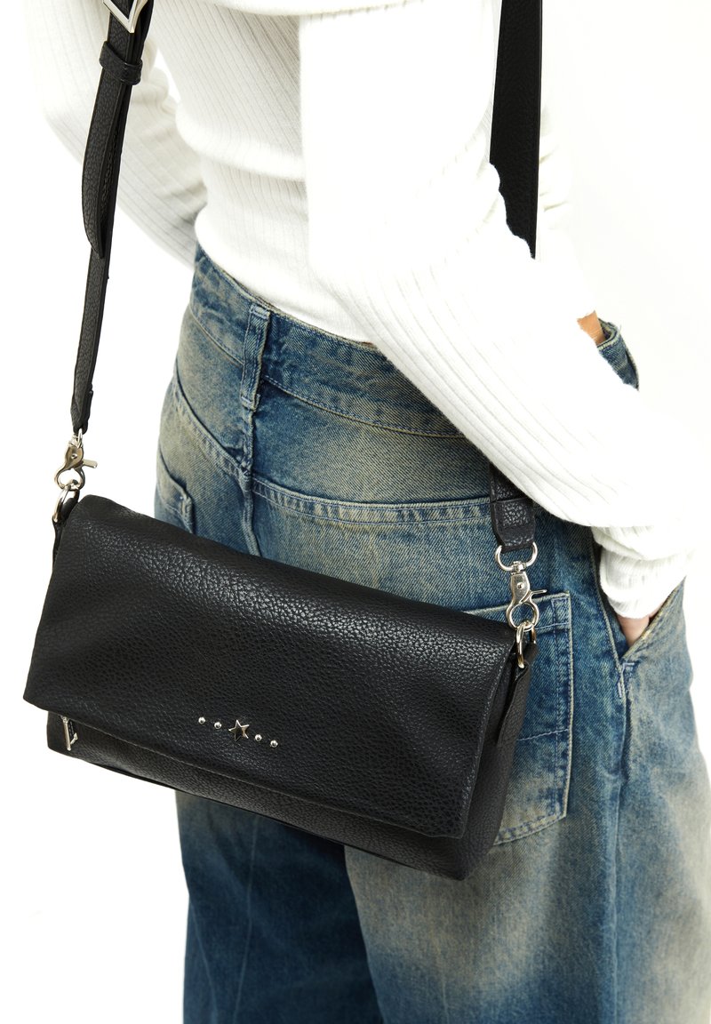 Borsa a tracolla in pelle nera con finitura testurizzata, forma rettangolare, dettagli in argento e tracolla regolabile, abbinata a jeans a vita alta.