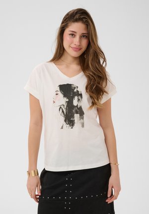 Ung kvinde med langt bølget hår iført en hvid t-shirt med et sort-hvidt profilansigttryk og et sort nederdel med nitter.