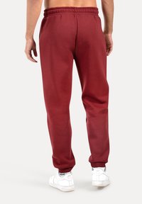 Bordeaux katoenen sweatpants met een elastische tailleband, taps toelopend bij de enkels, gecombineerd met witte sneakers. Gladde textuur, basisontwerp.