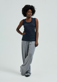 Sort tanktop med volanter i kanten, parret med løse, grå jersey joggingbukser. Glat tekstur, afslappet pasform og uformelt design.