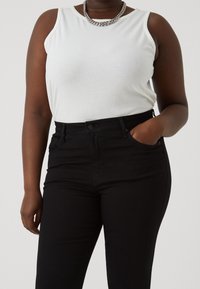 Top de tirantes blanco acanalado combinado con vaqueros negros de cintura alta, con costuras en contraste y bolsillos delanteros. Acento de collar de cadena plateada.