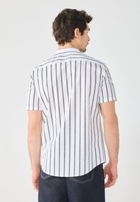 Camicia a maniche corte con colletto, di colore bianco con strisce verticali nere. Presenta un orlo arrotondato e una texture liscia.