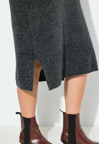 Jupe en tricot gris avec fente sur le côté, en tissu texturé, associée à des bottes de cheville en cuir marron avec des inserts élastiques noirs. Design à talon plat.