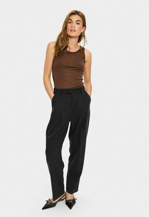 Haut sans manches marron, pantalon taille haute gris avec des plis, et chaussures noires à bout pointu avec des accents en forme de nœud. Texture plate dans l'ensemble.