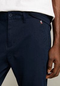Pantaloni blu navy realizzati in morbido tessuto misto cotone. Presentano una chiusura con bottone, tasche laterali e una piccola etichetta tricolore sul cinturino.