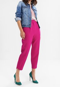 Chaqueta vaquera azul claro, ajustada con las mangas dobladas; pantalones de sastre color rosa intenso; zapatos de tacón altos color azul verdoso; camiseta floral debajo.