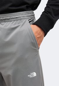 Άτομο που φορά γκρι παντελόνια The North Face με ελαστική μέση και χέρι στην τσέπη, συνδυασμένα με μαύρο μακρυμάνικο τοπ.