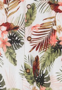 Floraler Stoff mit großem grünem Laub und rosa Blumen, verziert mit braunen Knöpfen an der Vorderöffnung. Die Textur wirkt leicht.