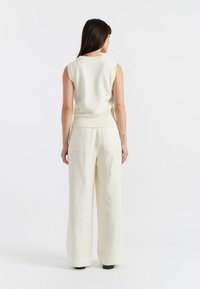 Ärmelloses Strickoberteil in Off-White aus texturiertem Stoff, mit geripptem Ausschnitt. Kombiniert mit lässigen Off-White Hosen mit Gesäßtaschen.