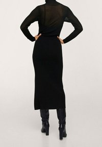Robe noire à manches longues avec une silhouette ajustée, panneau arrière transparent, fente latérale, associée à des bottes noires à talons hauts jusqu'aux genoux.
