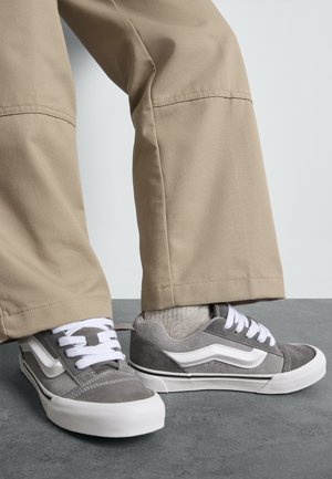 Graue lässige Sneakers mit weißen Schnürsenkeln und seitlichen Akzenten, gefertigt aus Wildleder und Canvas. Tragen Sie sie zu beigefarbenen Hosen. Flache Gummisohle.