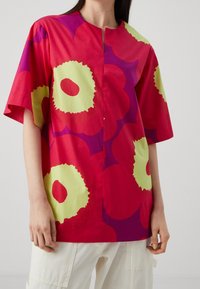 Rød kortærmet top med store abstrakte blomster i grøn og lilla. Har en rund halsudskæring og en afslappet pasform. Fremstillet af bomuldsstof.