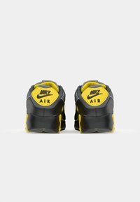 Black and yellow Nike Air shoes, viewed from the back, featuring the logo prominently on the heel and a textured sole.