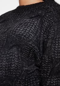 Svart stickad tröja med en strukturerad kabelmönster, rund hals och lös passform. Tillverkad av ett mjukt, varmt garn med varierande tjocklek.
