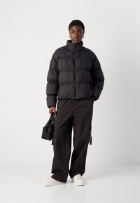 Svart boblejakke med høy krage, glidelåsbeslag og kviltet tekstur. Kombinert med mørke cargo-bukser og hvite sneakers. Liten svart veske.