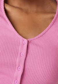Detailní záběr na hruď osoby oblečené v růžovém žebrovaném topu s knoflíky a výstřihem do V.