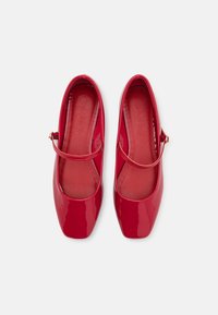 Zapatos Mary Jane de charol rojo con punta cuadrada y una correa delgada en el empeine, con un detalle de hebilla dorada.