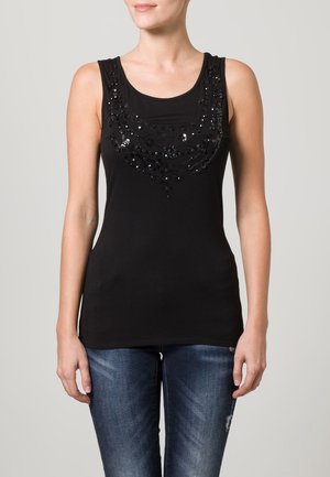 Czarny top na ramiączkach z dekoltem w kształcie litery U, ozdobiony cekinami tworzącymi wzór na wysokości klatki piersiowej. Połączony z niebieskimi dżinsami.