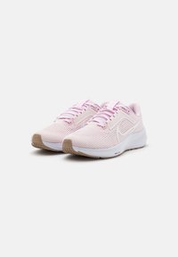 Zapatillas de running Nike en rosa claro con suelas blancas y detalles texturizados en marrón en la punta y el talón, exhibidas una al lado de la otra sobre un fondo blanco.