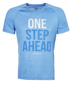 Mężczyzna ubrany w niebieską koszulkę z napisem "ONE STEP AHEAD", czarne sportowe szorty i szare buty do biegania, stojący na jasnoszarym tle.