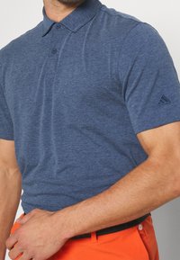 Laivastonsininen lyhythihainen poolopaita, valmistettu teksturoidusta kankaasta; siinä on kolmipainikkeinen nappilista ja vasemmassa hihassa logotunnus.